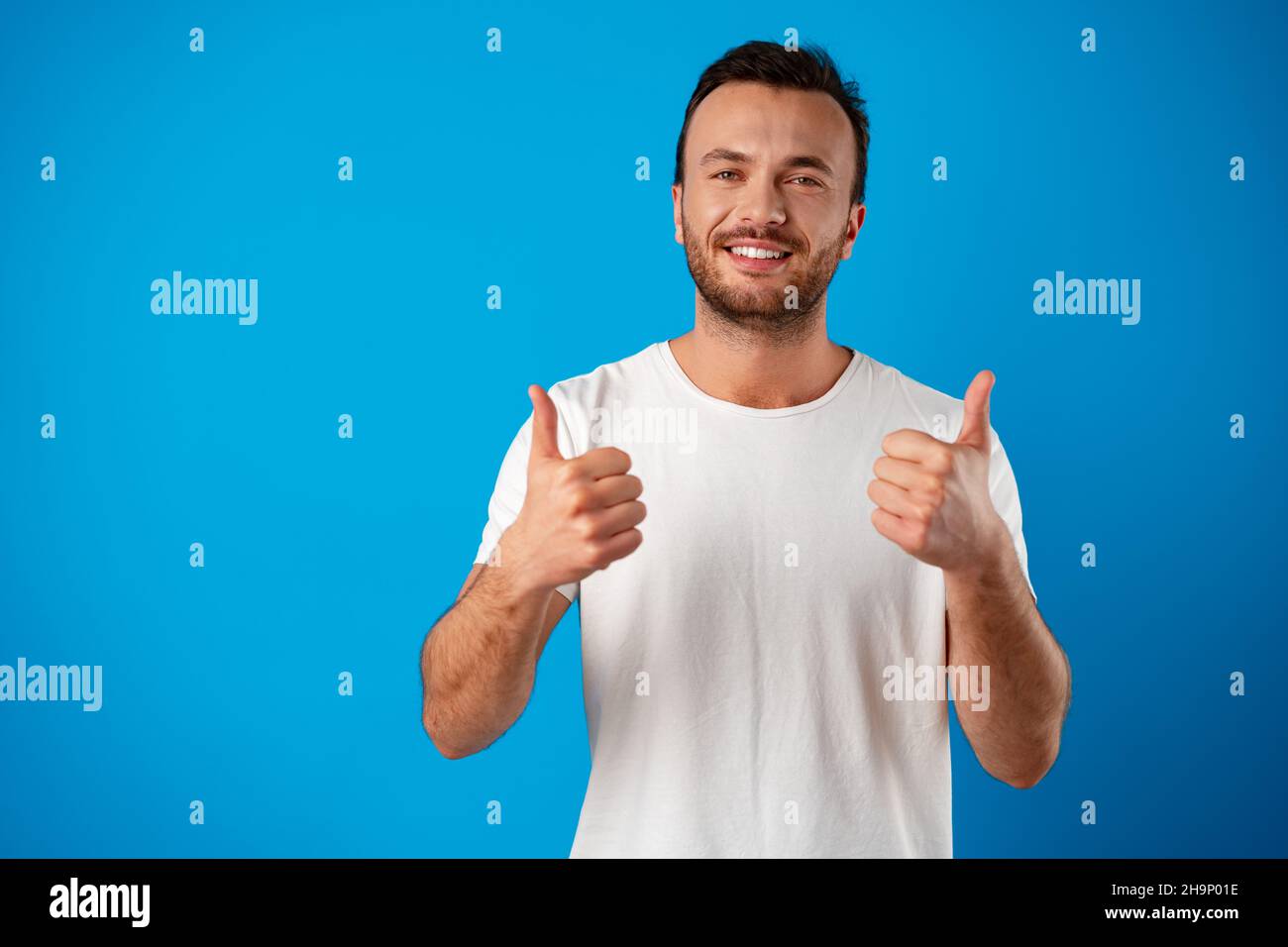 Portrait of cheerful man smiling and showing thumb up over blue background Stock Photo