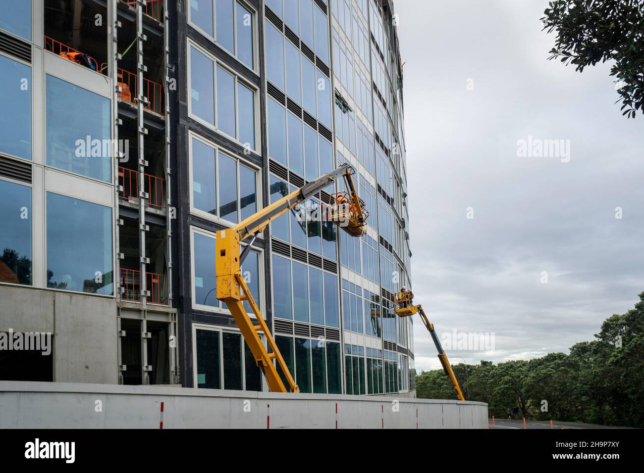 Apartment under construction. Builders wearing face masks working on yellow crane, Milford, Auckland. Stock Photo