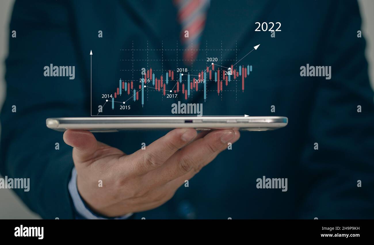 Businessman holding tablet 2022 stock market forecast outlook, charts and candlesticks, stock market movement trend, past to present. Stock Photo