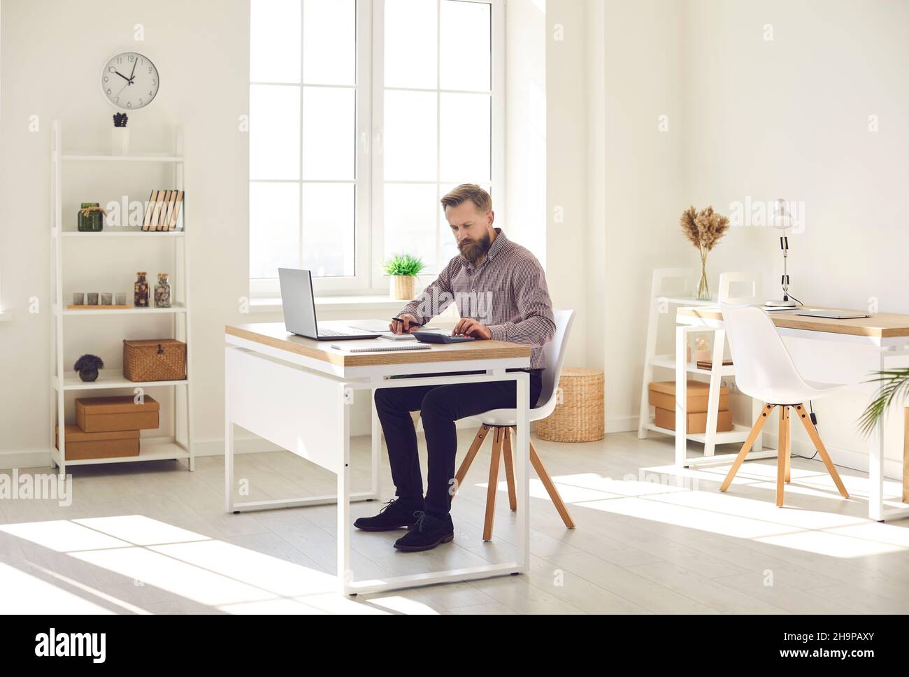 Man working in his office, sitting at desk with laptop computer and using calculator Stock Photo