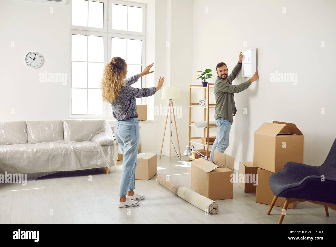 Happy couple hanging a picture on the wall while unpacking boxes in their new house Stock Photo