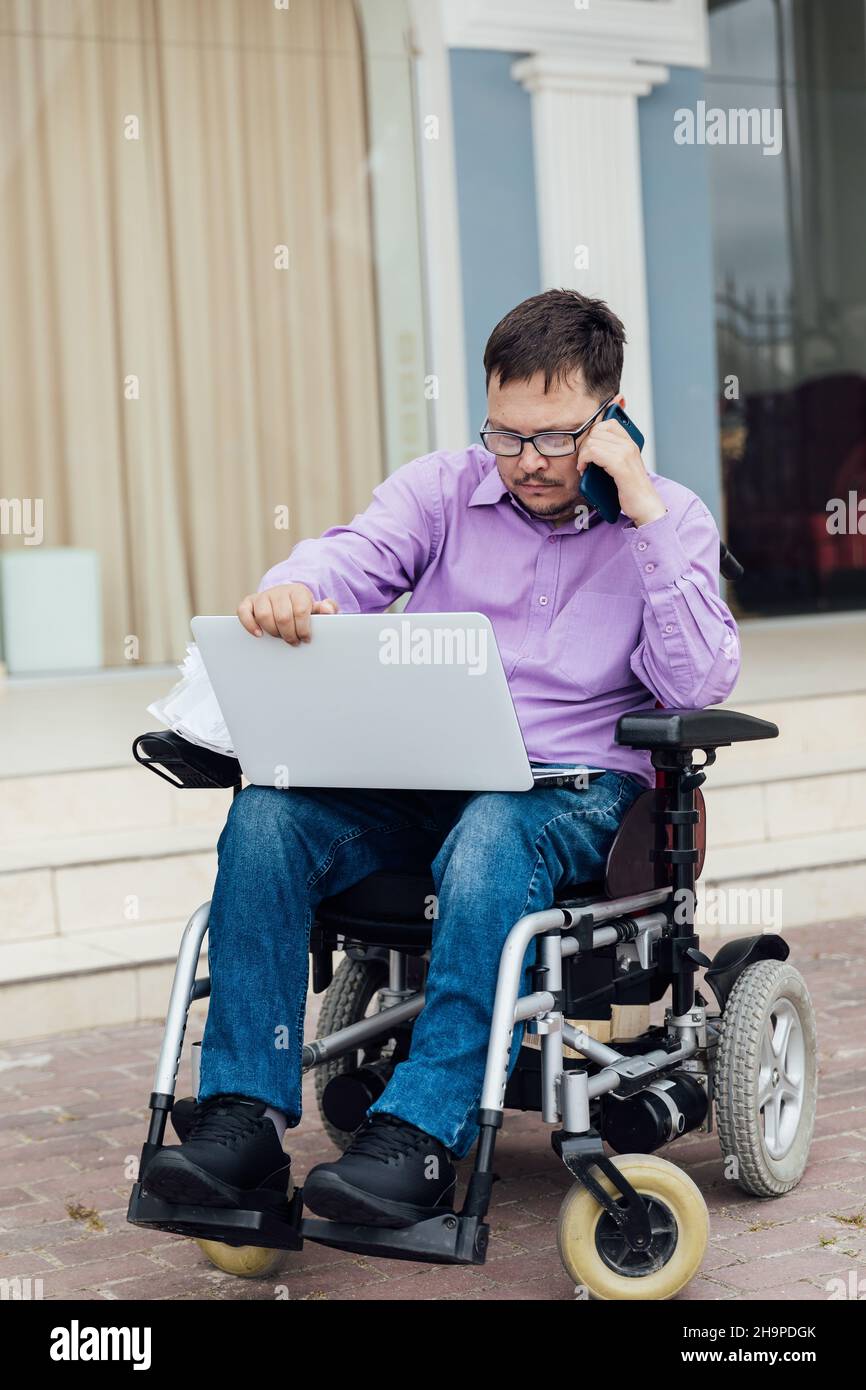 a man with disabilities in a wheelchair works on a laptop Stock Photo
