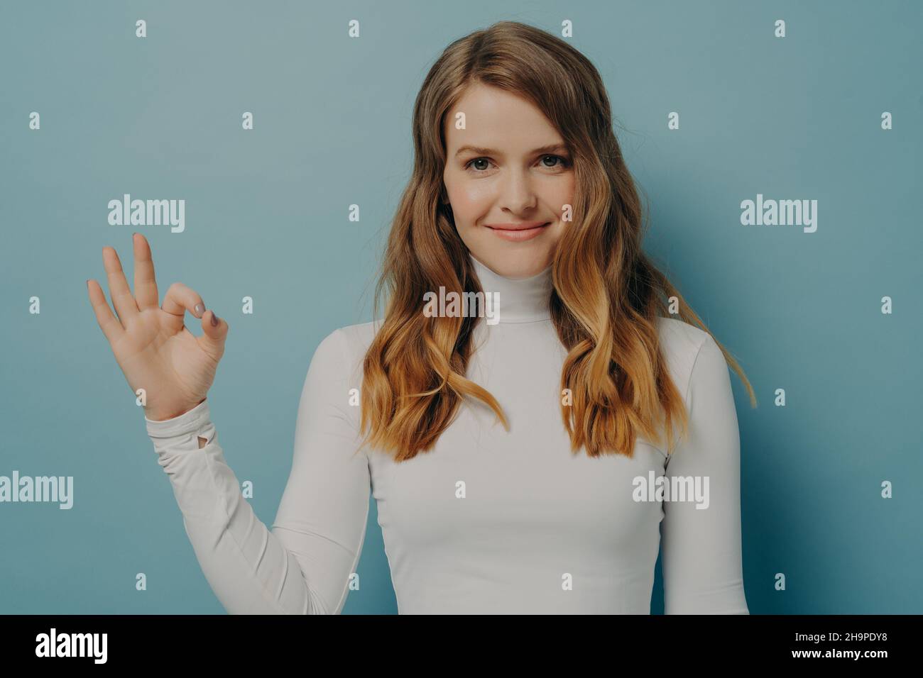 Cheerful young european woman showing okay gesture isolated over pastel blue studio wall Stock Photo