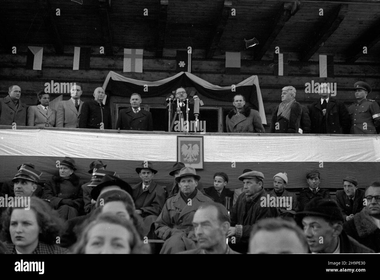 Zakopane, 1949-02-23. Od 23 lutego do 3 marca odbywa³y siê Miêdzynarodowe Zawody Narciarskie o Puchar Tatr. Zgromadzi³y one kilkudziesiêciu sportowców z Polski, Bu³garii, Czechos³owacji, Finlandii, Rumunii i Wêgier. Pierwszego dnia, na stadionie Pod Krokwi¹, odby³o siê uroczyste otwarcie zawodów. Nz. dyrektor G³ównego Urzêdu Kultury Fizycznej Tadeusz Kuchar (5P) przemawia na otwarciu zawodów. Obok niego m.in.: wojewoda krakowski Kazimierz Pasenkiewicz (5L) i wiceprezes Polskiego Zwi¹zku Narciarskiego Aleksander Boniecki (4L). pw PAP Zakopane, Feb. 23, 1949. International Skiing Competiti Stock Photo