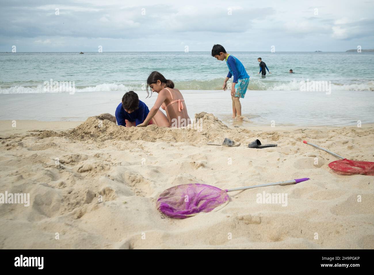 kids playing on the sandy beach making sand castle in a cloudy weather next to a wavy sea Stock Photo