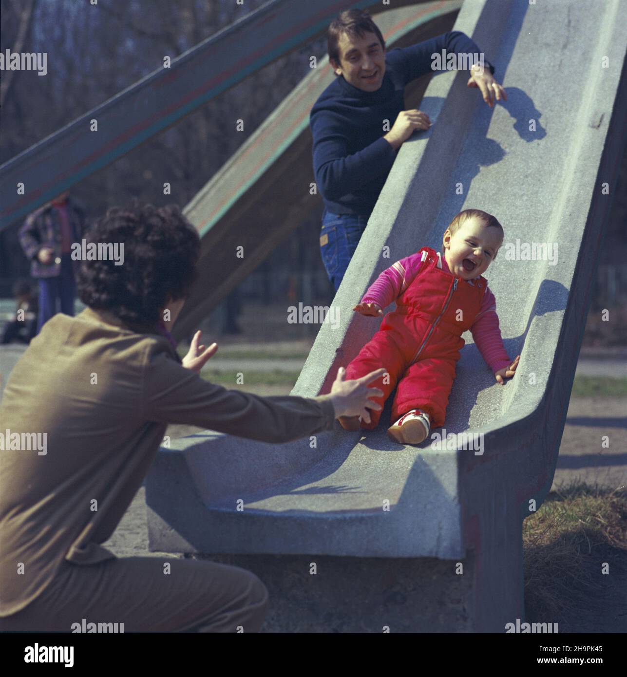 Warszawa 04.1980. Rodzina na spacerze w parku. Nz. zabawa z dzieckim na zje¿d¿alni. mw  PAP/Jan Morek    Dok³adny dzieñ wydarzenia nieustalony.         Warsaw, April 1980. Parents and child play on a slide in a park playground.  mw  PAP/Jan Morek    Event day unknown Stock Photo