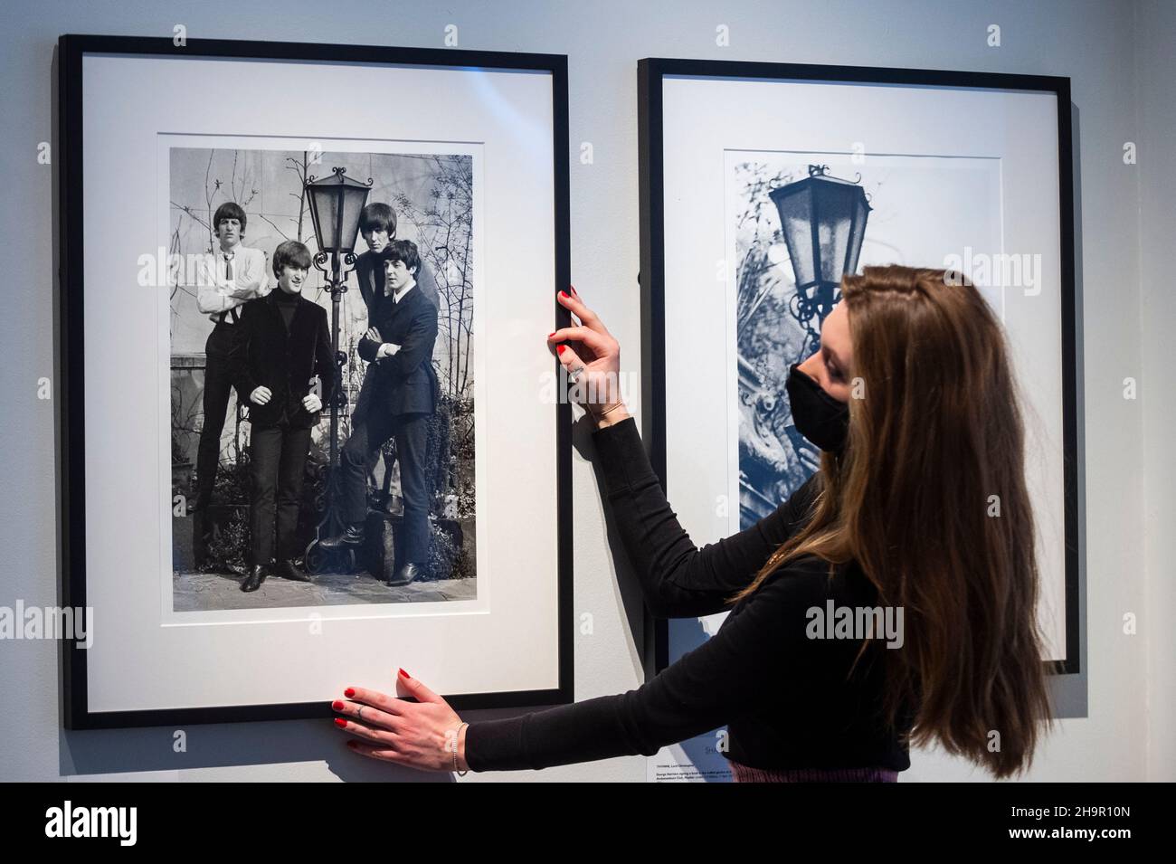 London, UK.  8 December 2021.  A staff member with a photo of the band at the preview of an exhibition of lost photographs of The Beatles by Lord Thynne, son of the 6th Marquess of Bath.  The exhibition, featuring candid images of the band in spring 1964 on the set of their first film A Hard Day’s Night, is at the Shapero Modern Gallery in Mayfair until 16 January 2022. Credit: Stephen Chung / Alamy Live News Stock Photo