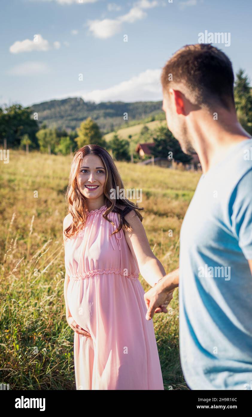 Happy couple expecting baby holding hands. Smiling pregnant woman following her husband Stock Photo
