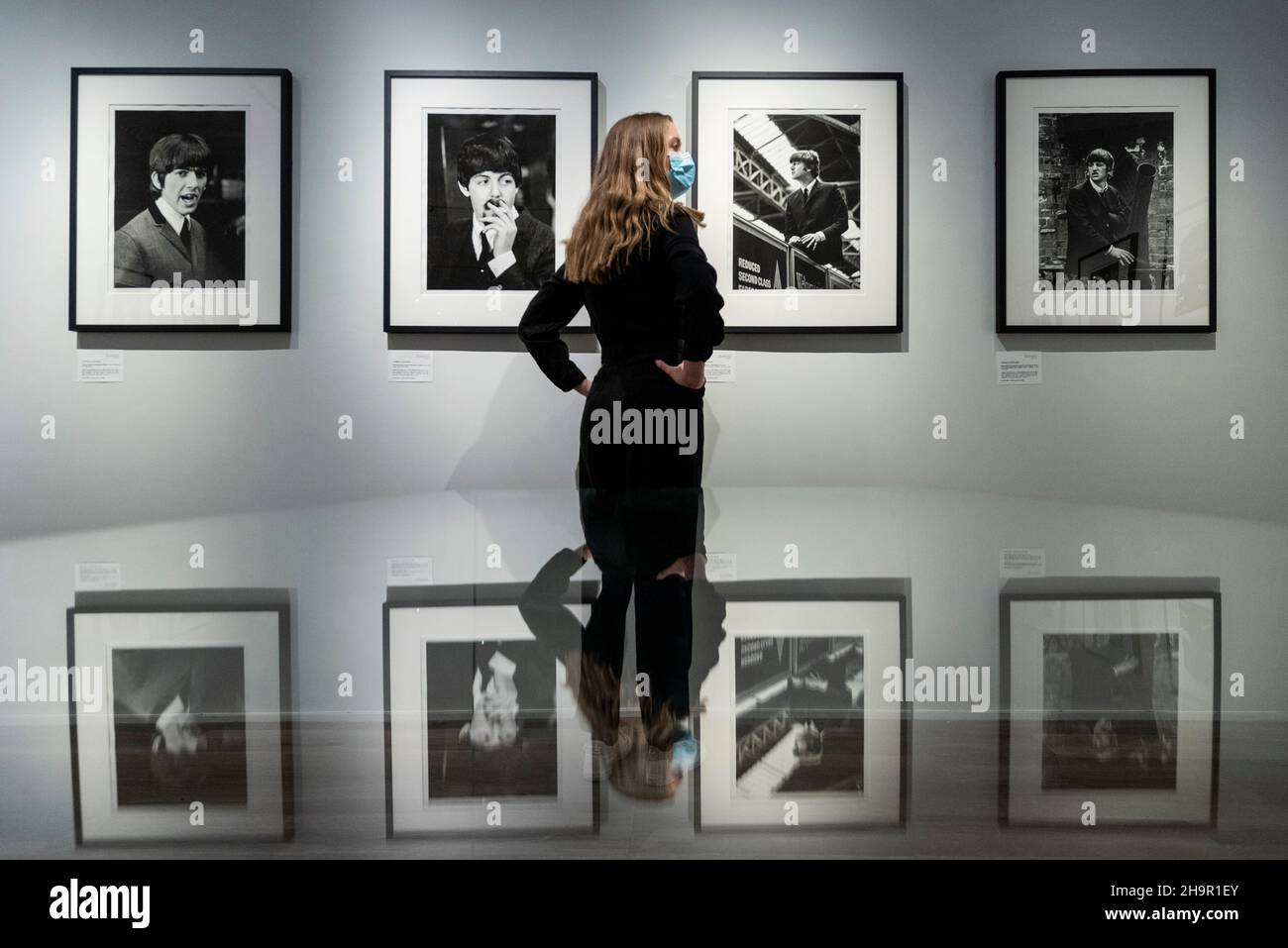 London, UK.  8 December 2021.  A staff member next to photos of George Harrison, Paul McCartney, John Lennon and Ringo Starr at the preview of an exhibition of lost photographs of The Beatles by Lord Thynne, son of the 6th Marquess of Bath.  The exhibition, featuring candid images of the band in spring 1964 on the set of their first film A Hard Day’s Night, is at the Shapero Modern Gallery in Mayfair until 16 January 2022. Credit: Stephen Chung / Alamy Live News Stock Photo