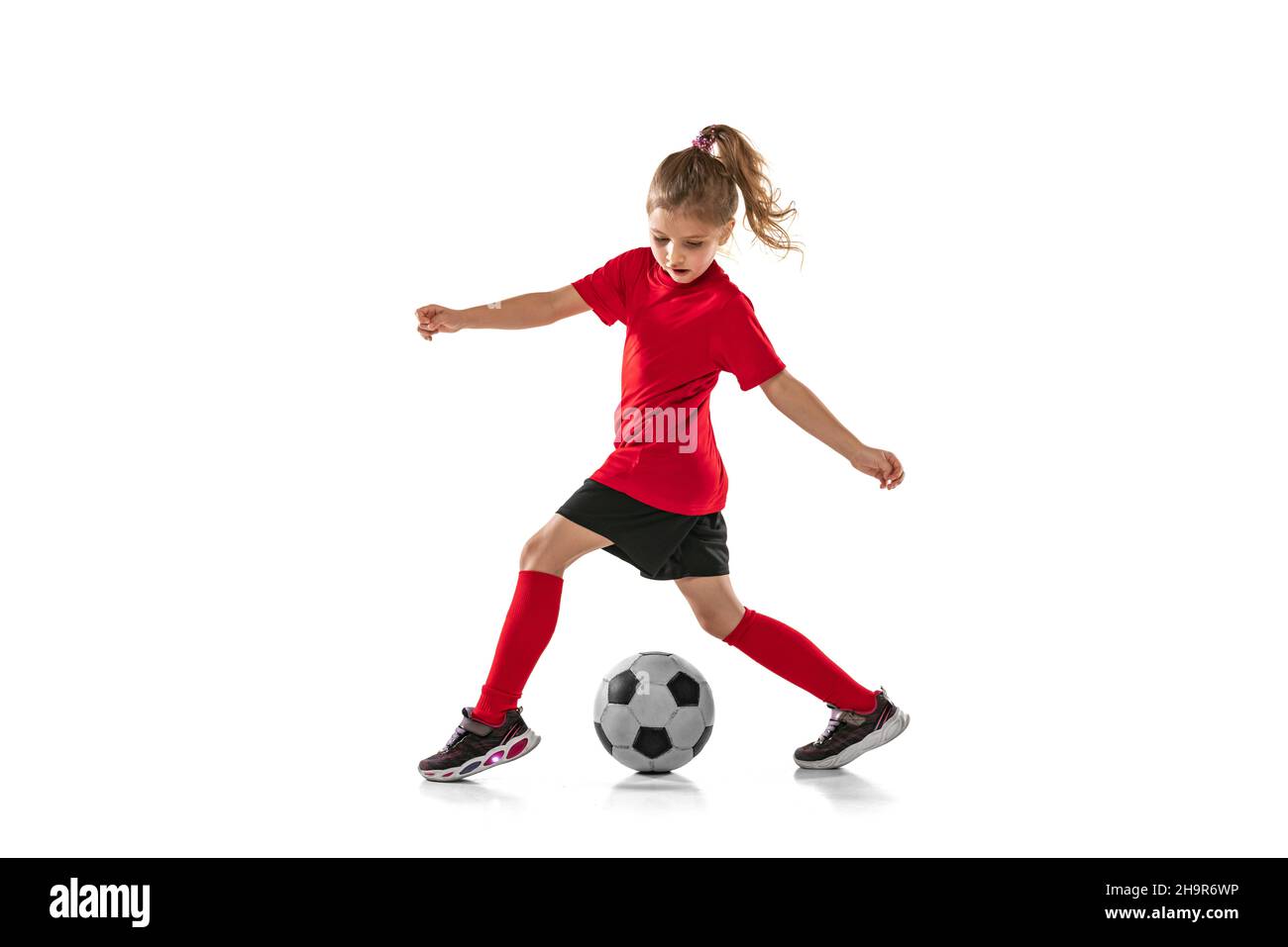 Fulllength portrait of little girl, child playing football, training, dribbling ball isolated