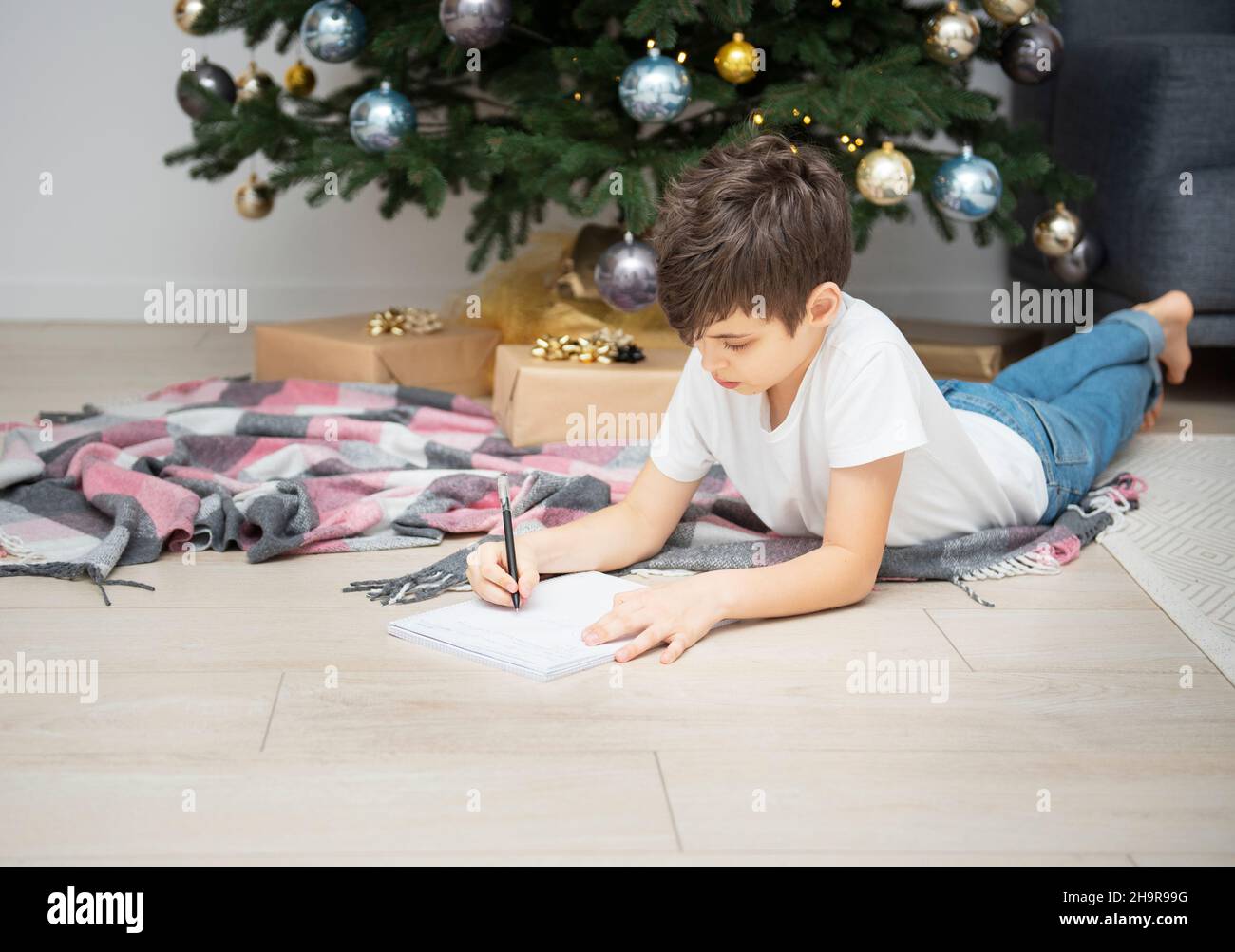 Boy writes letters to Santa Claus near the Christmas tree in the living ...