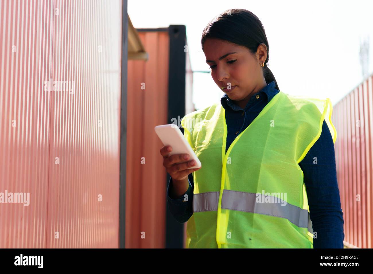 Portrait of a woman checking her cell phone while working in a distribution warehouse. Stock Photo