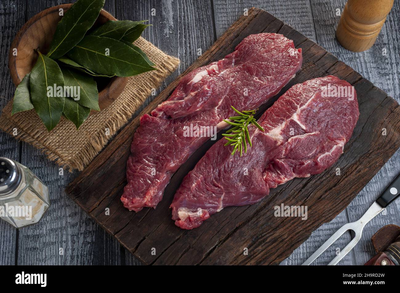 Raw striploin beef steaks with rosemary, bay leaves, salt, and meat