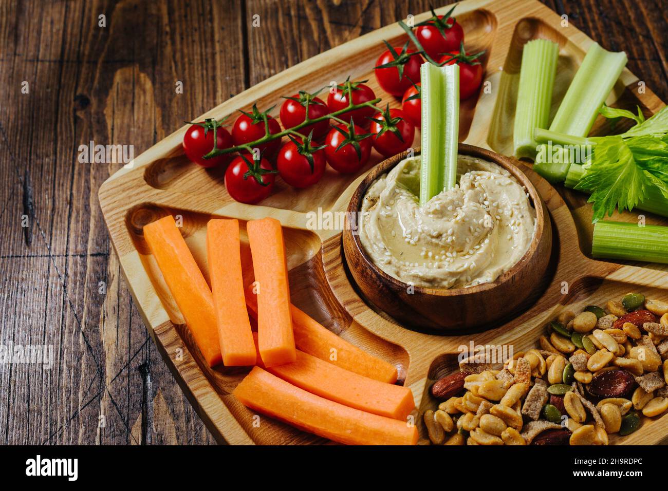Hummus and vegetable sticks of carrot and celery on a wooden plate