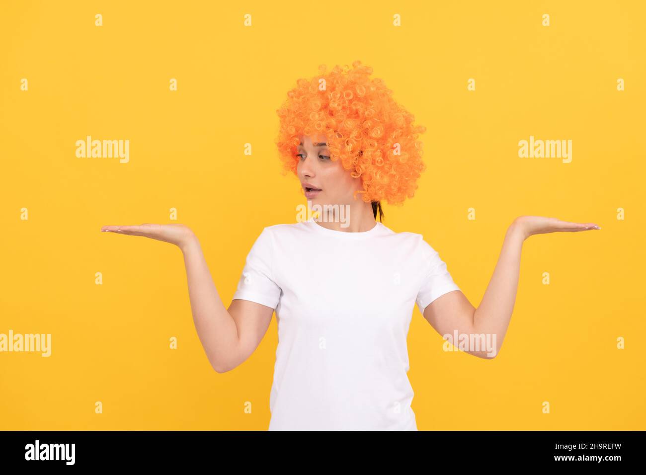 amazed funny girl with fancy look wearing orange hair wig presenting product, copy space, choice. Stock Photo