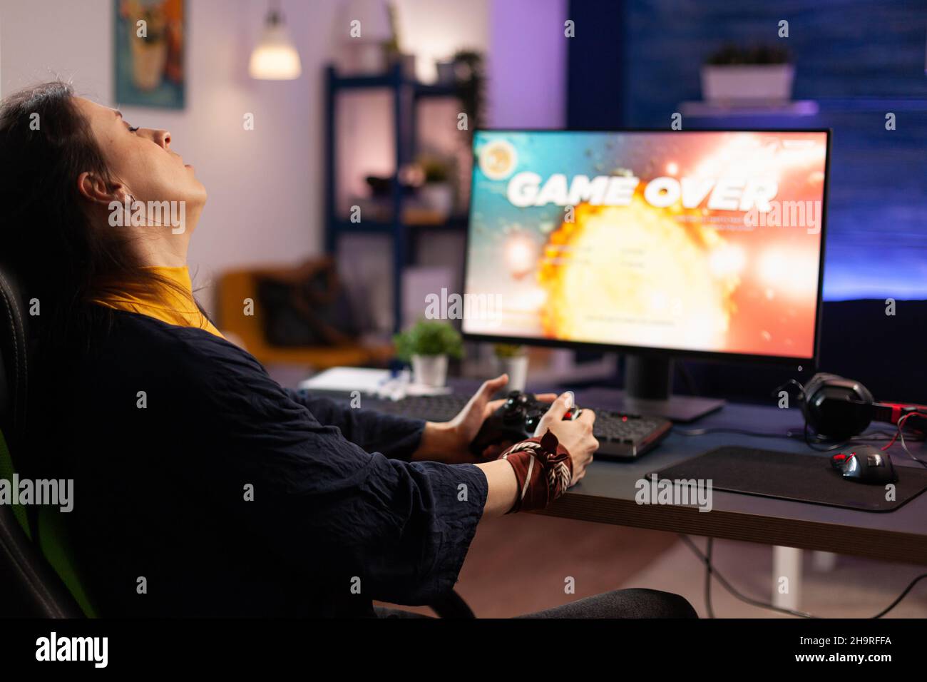 Disappointed adult losing online video games on computer. Frustrated woman playing on monitor, using modern controller and feeling sad about lost game. Gamer with electronic e sport. Stock Photo