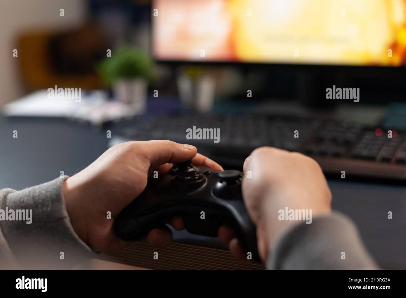 Close up of player holding joystick, losing video games in front of computer. Gamer using joystick and playing online games on monitor, sitting at desk. Man gaming with modern equipment. Stock Photo
