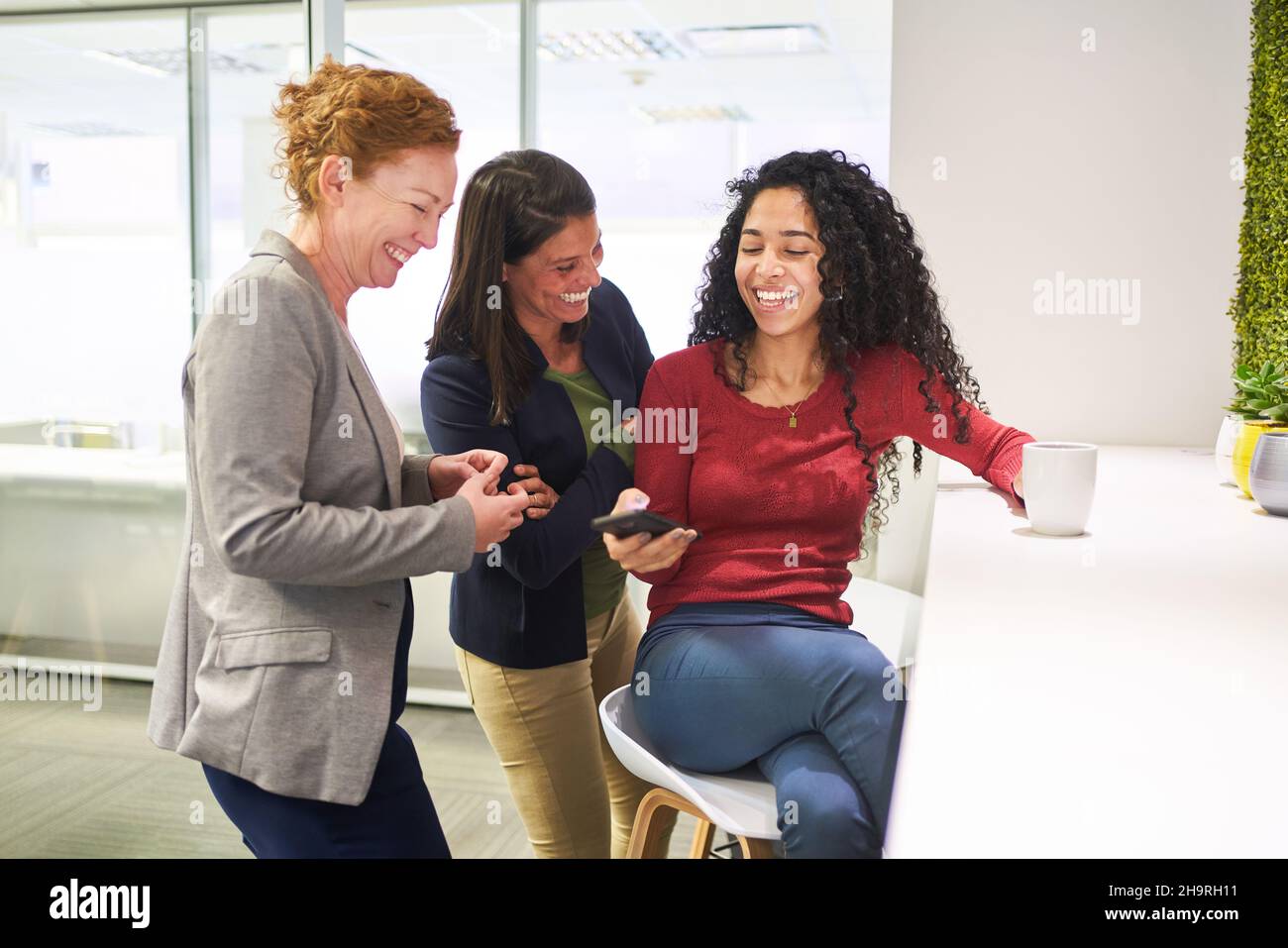 Women laugh together over a text message or email on their smartphones during a break Stock Photo