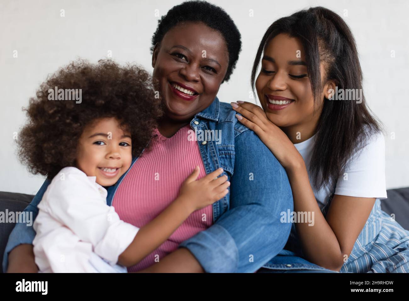 happy african american granny smiling at camera while daughter and granddaughter hugging her at home Stock Photo