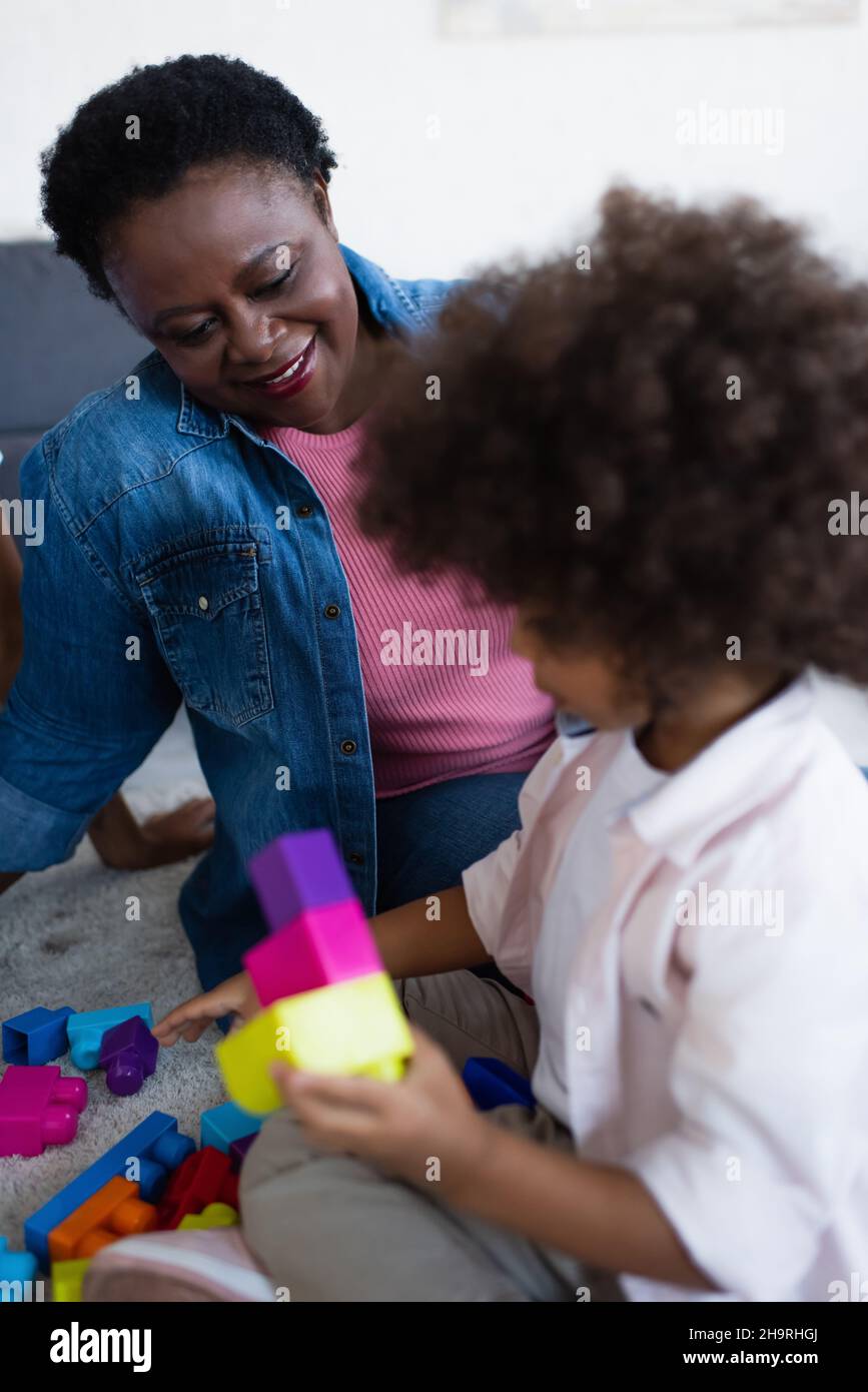 smiling african american granny looking at blurred granddaughter playing with building blocks Stock Photo
