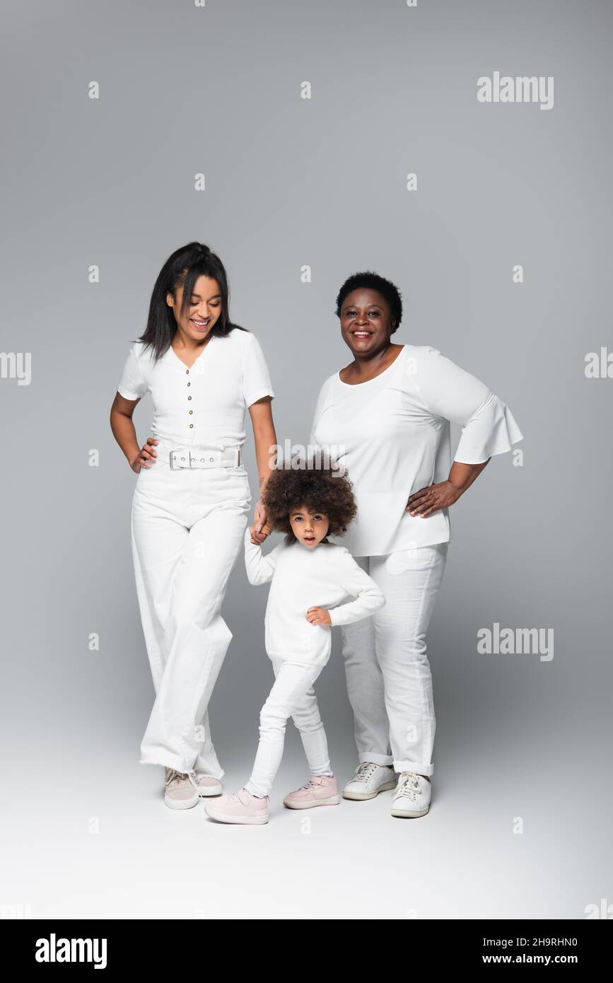 smiling african american women and girl in white clothes posing with hands on hips on grey Stock Photo