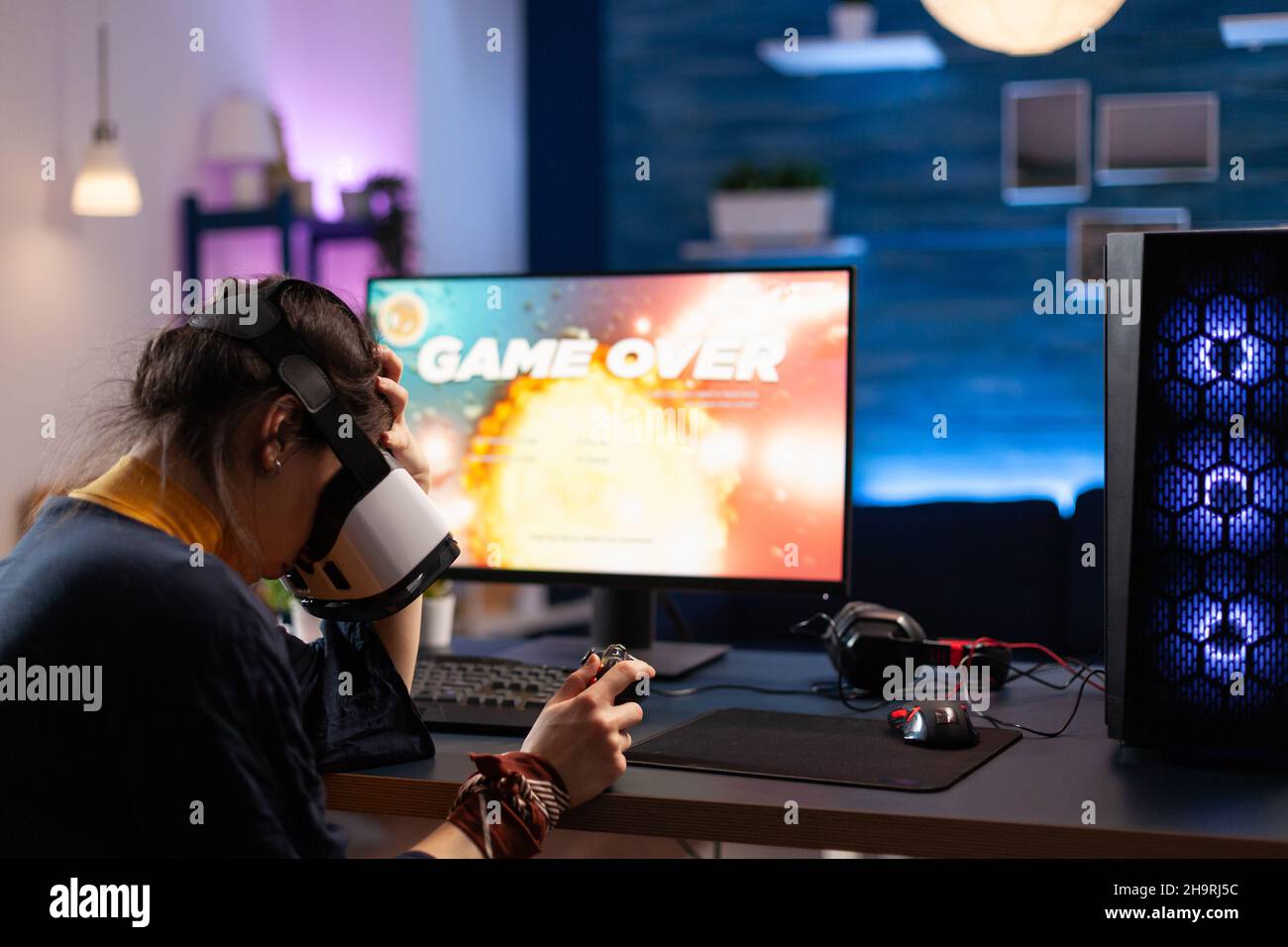 Woman using vr glasses to play online video games and losing on computer. Person playing game with controller on monitor and virtual reality headset. Adult with gaming equipment. Stock Photo