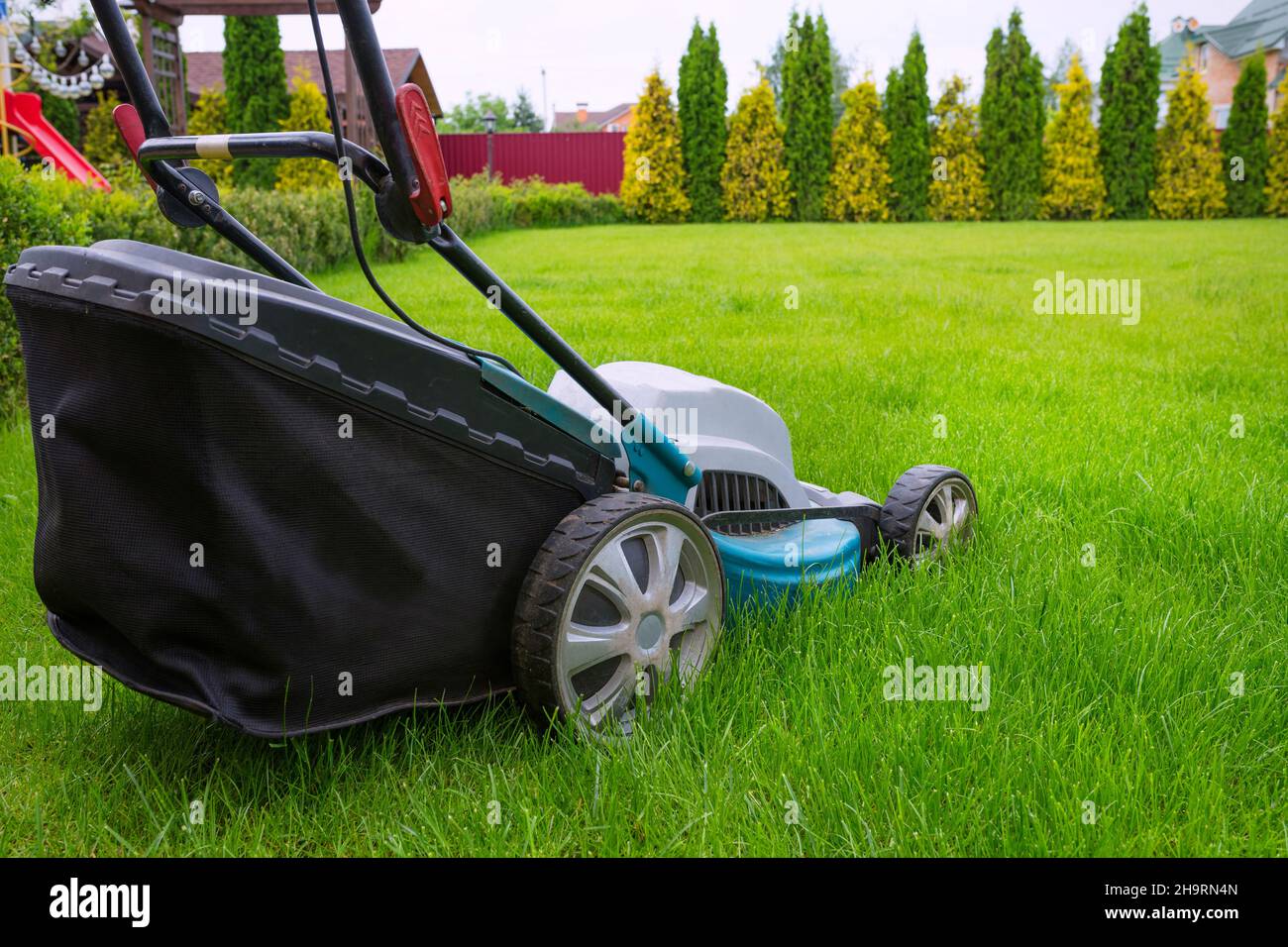 A lawn mower mowing green grass in the house backyard. A closeup of an