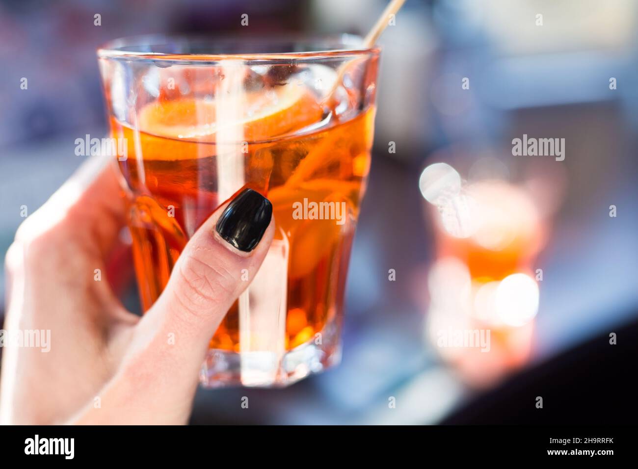 Glass with orange spritz in sunny day. Female hand with black nails. Serving drinks outdoors. Isolation concept. Traditional venetian italian cocktail Stock Photo