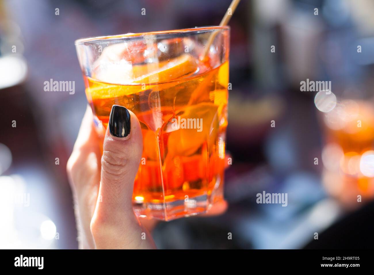 Woman holds a glass with orange spritz in sunny day. Hand with black nails. Serving drinks outdoors. Isolation concept. Traditional venetian italian Stock Photo