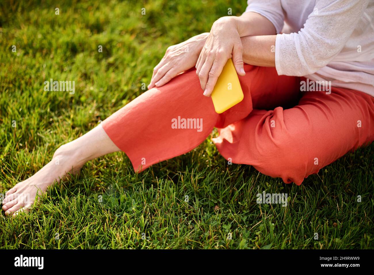 Woman with smartphone sitting on grass resting Stock Photo