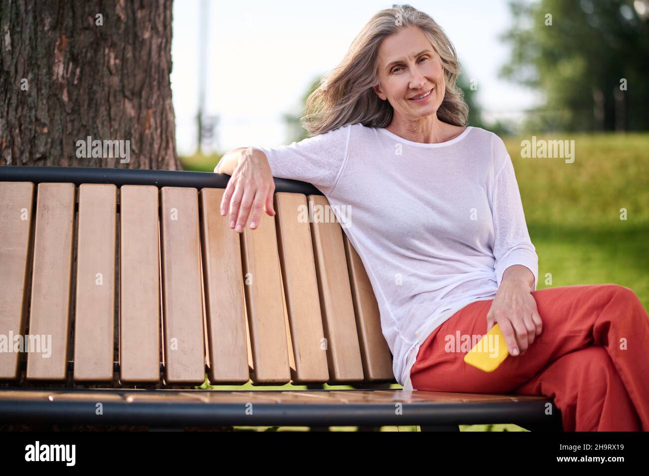 Woman with smartphone sitting on bench in park Stock Photo