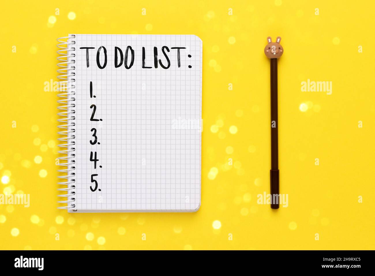 Open spiral squared notebook with to do list and brown pen with bunny head on bright yellow background with blurred lights bokeh, top view, flat lay Stock Photo