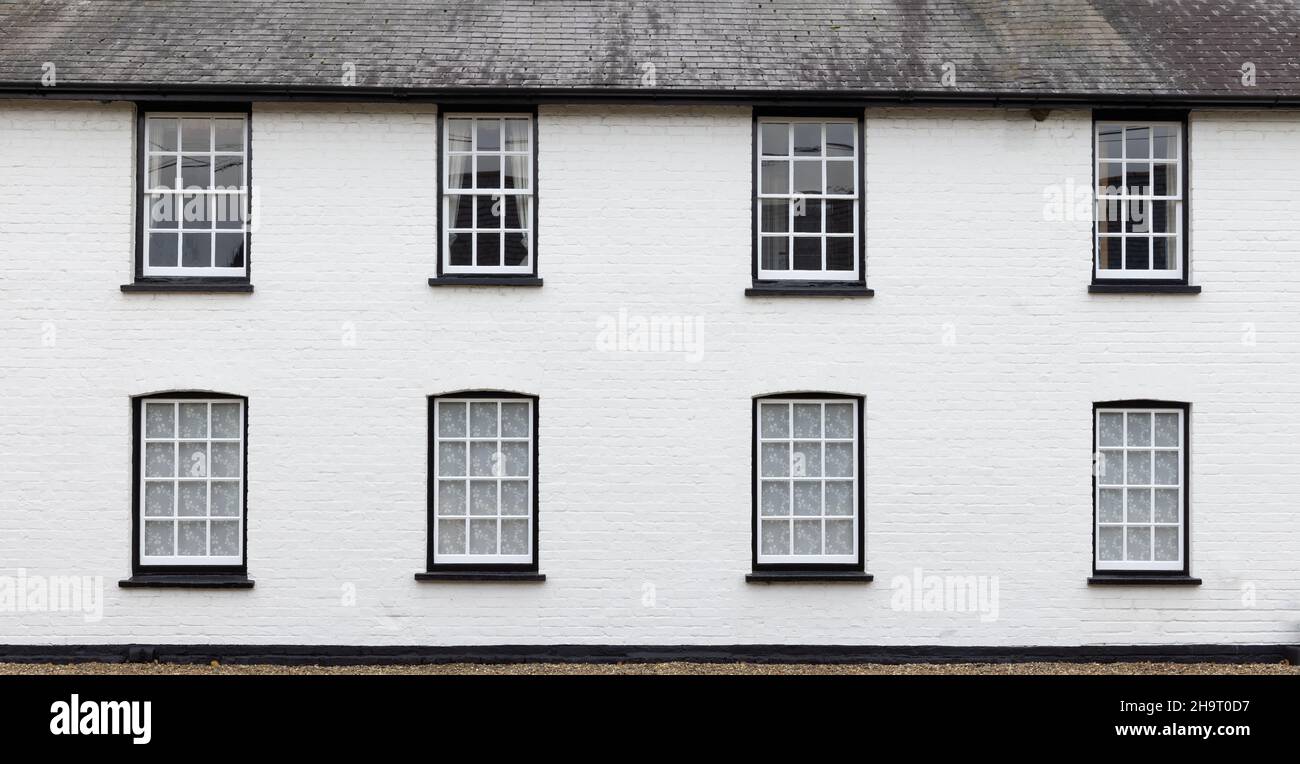 Side of an old house with white brick wall with Victorian white wooden windows. UK Stock Photo