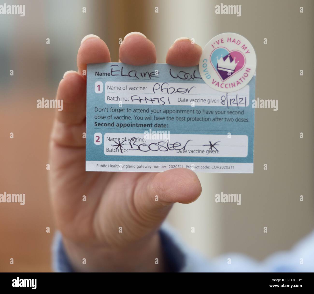 Hand holding COVID 19 vaccination card and sticker issued for their booster jab. Stock Photo
