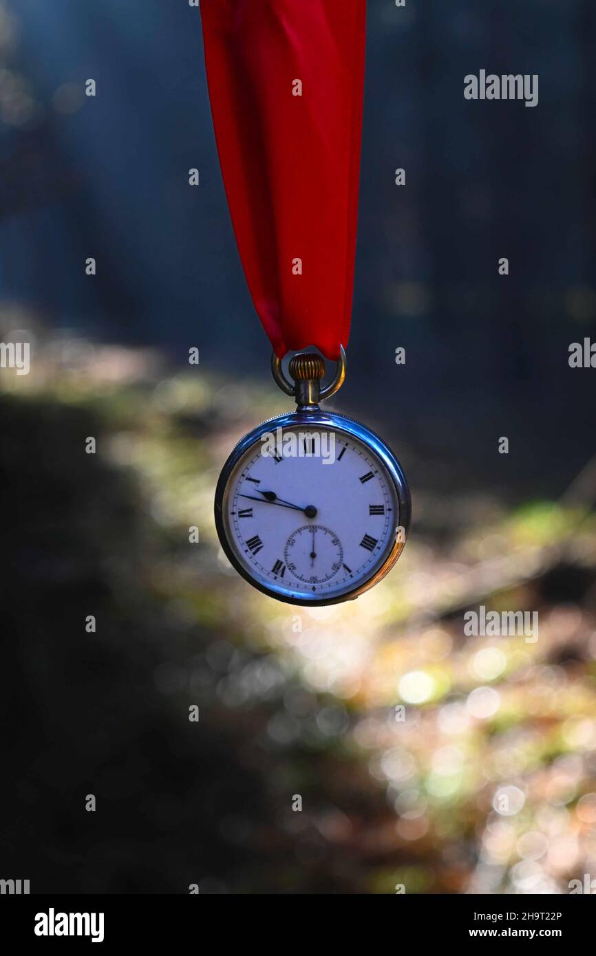 old silver pocket watch hanging from a red ribbon with abstract background. Stock Photo