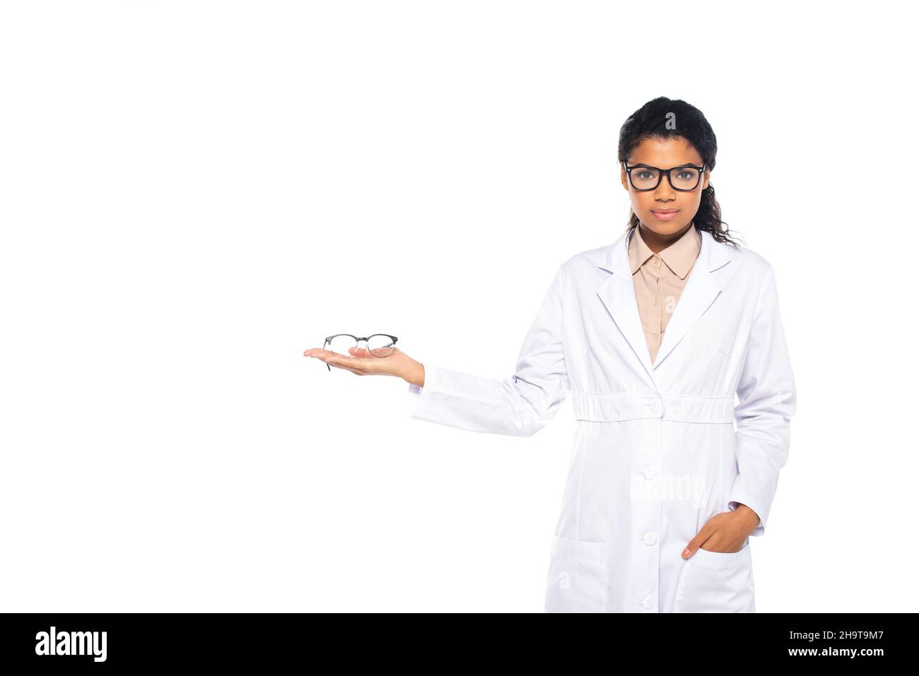 African american ophthalmologist holding eyeglasses and hand in pocket of white coat isolated on white Stock Photo