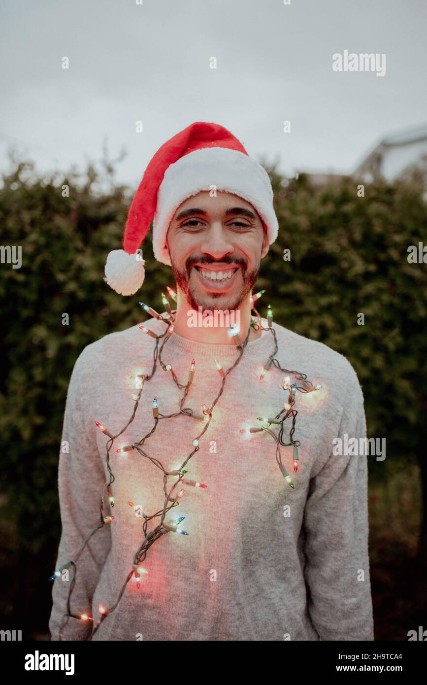 Mixedrace man laughs in santa hat and sweater wearing holiday lights