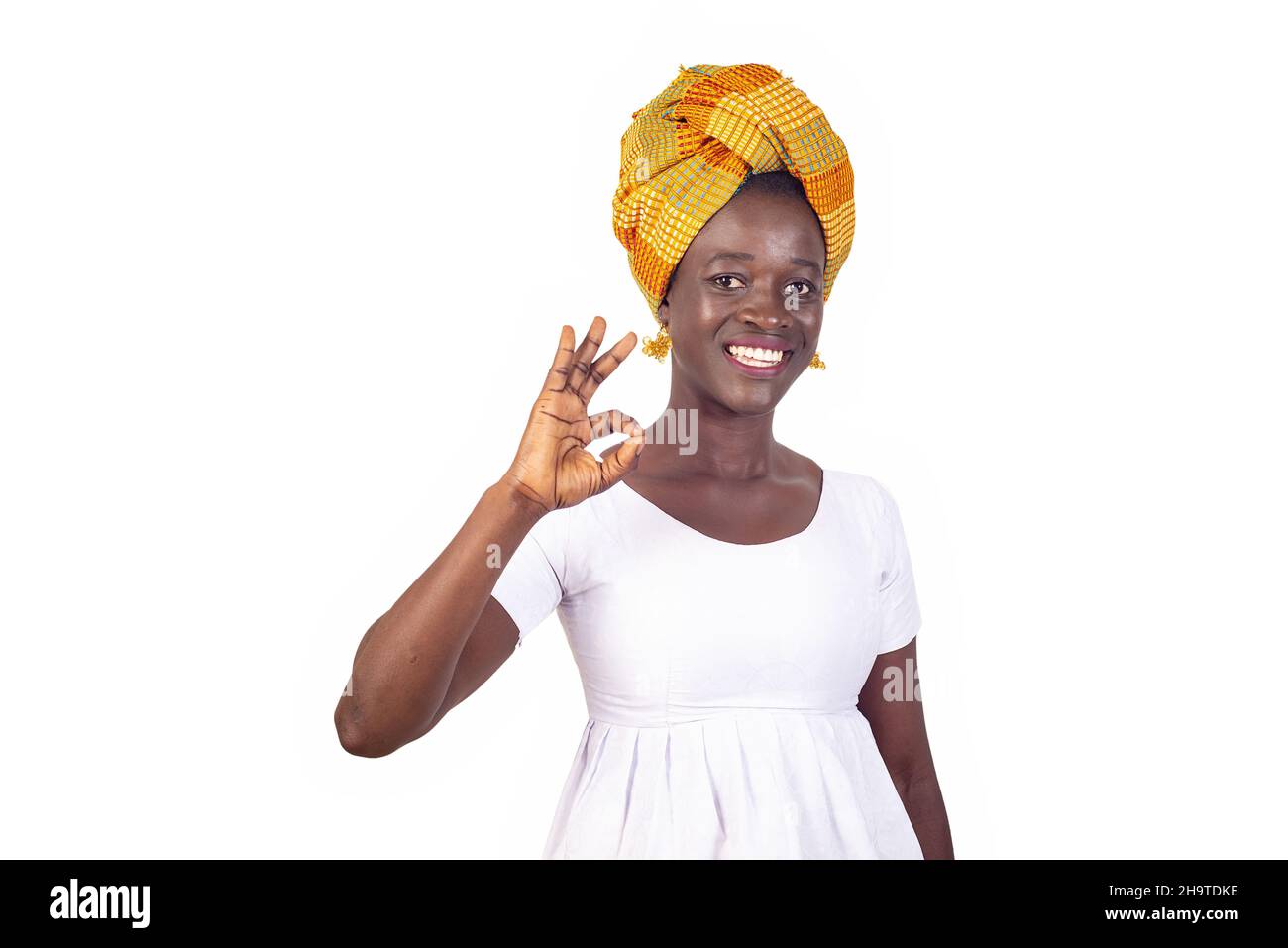beautiful young african woman in traditional dress standing on white background waving okay and looking at camera smiling. Stock Photo