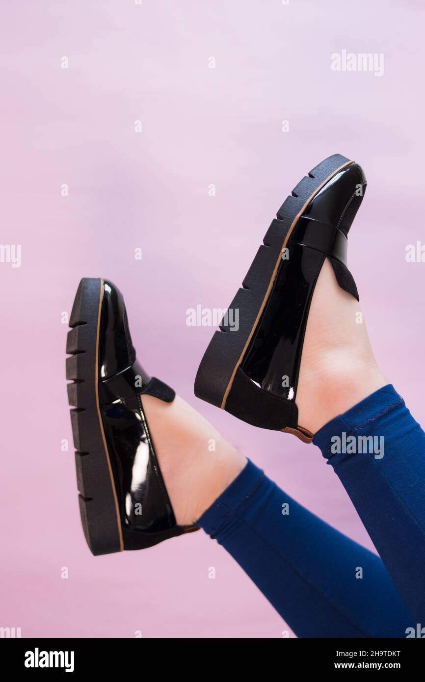 Caucasian feet wearing some black shoes and blue pant, on a pink background Stock Photo