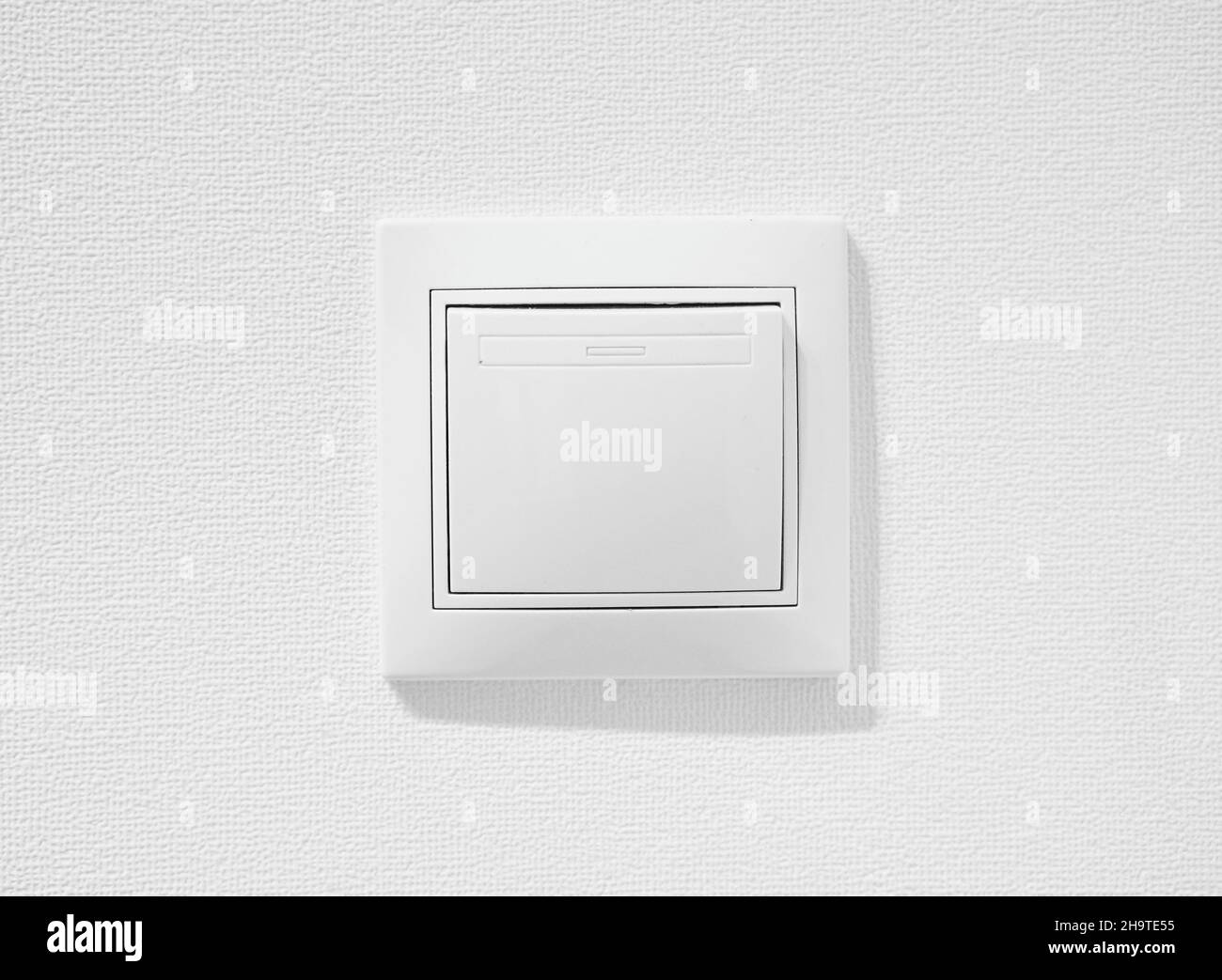 Cheap simple single-pole light switch. Inexpensive plastic push button switch against white wall. White common toggle switch in home. Standart rocker Stock Photo