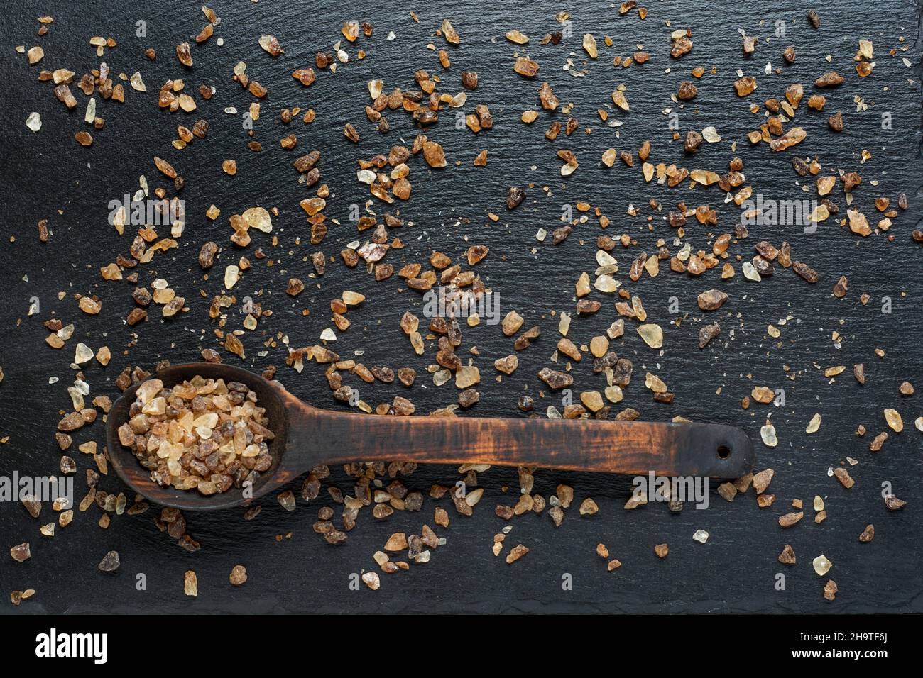 Wooden spoon full of dark brown granulated sugar on slate background close up. Stock Photo