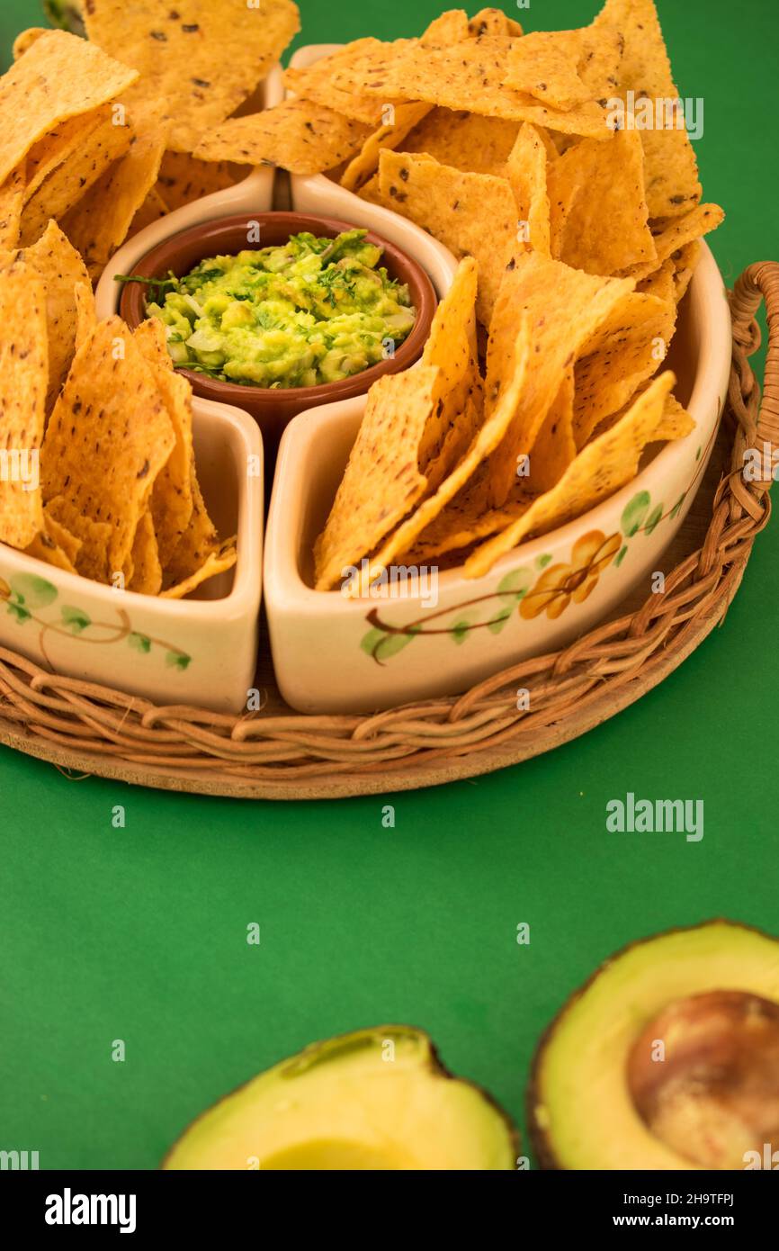 Some fried nachos in a pot with some fresh guacamole on a green surface Stock Photo