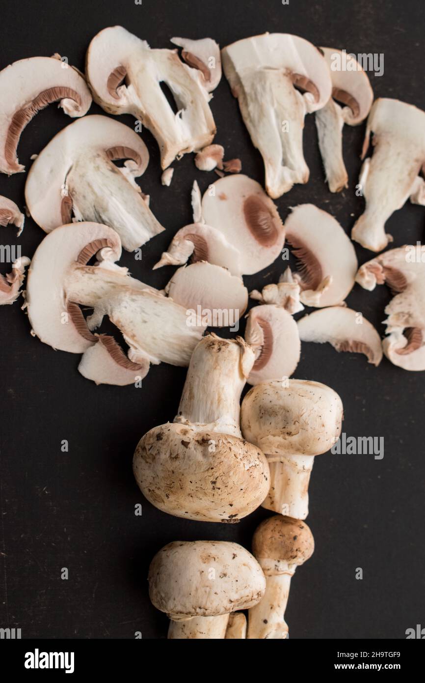 Cut champignon and some mushrooms in a basket with a knife on a black wooden table Stock Photo
