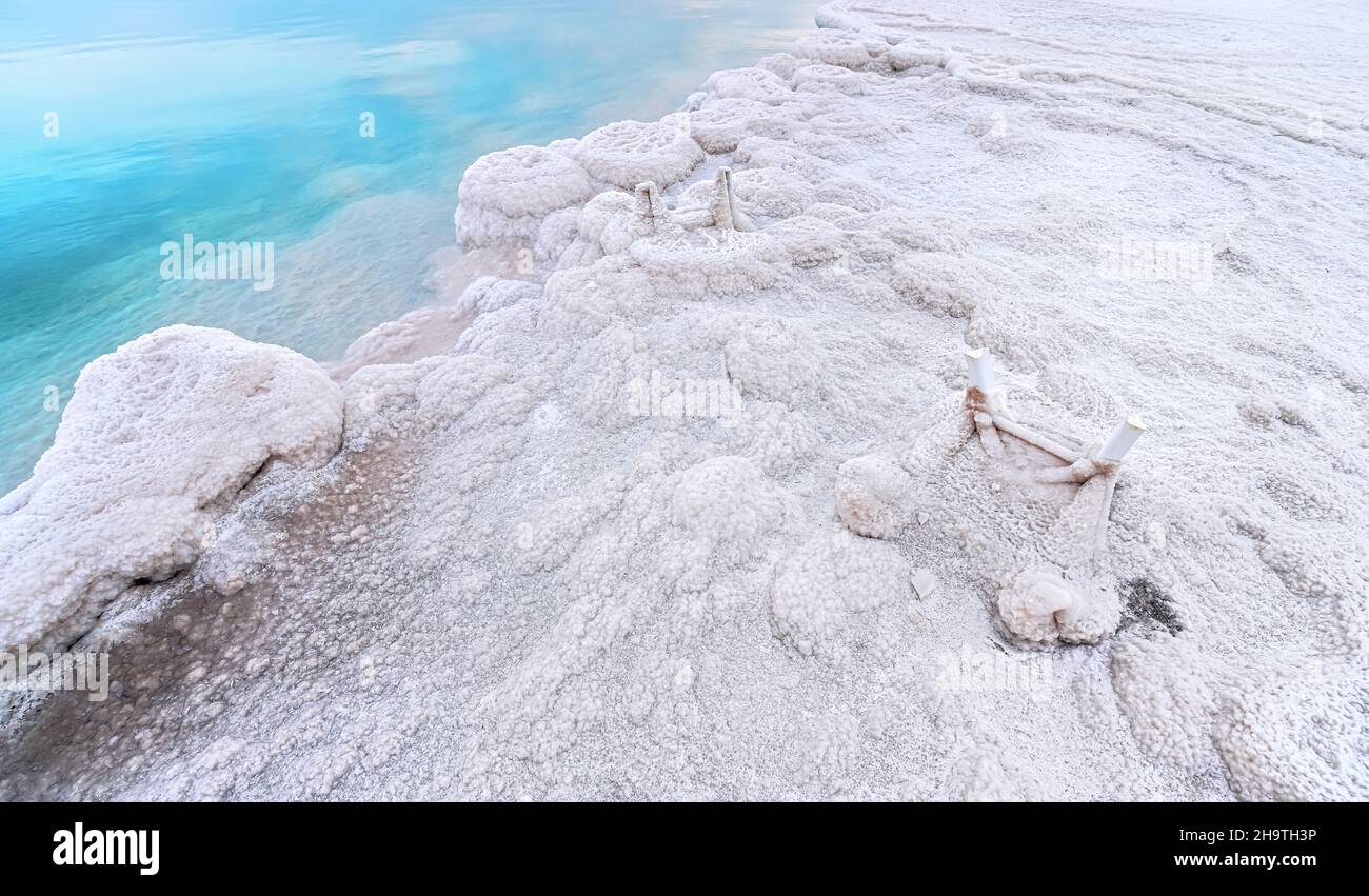 Small plastic chairs completely covered with crystalline salt on shore of dead sea, closeup detail, clear blue water near Stock Photo