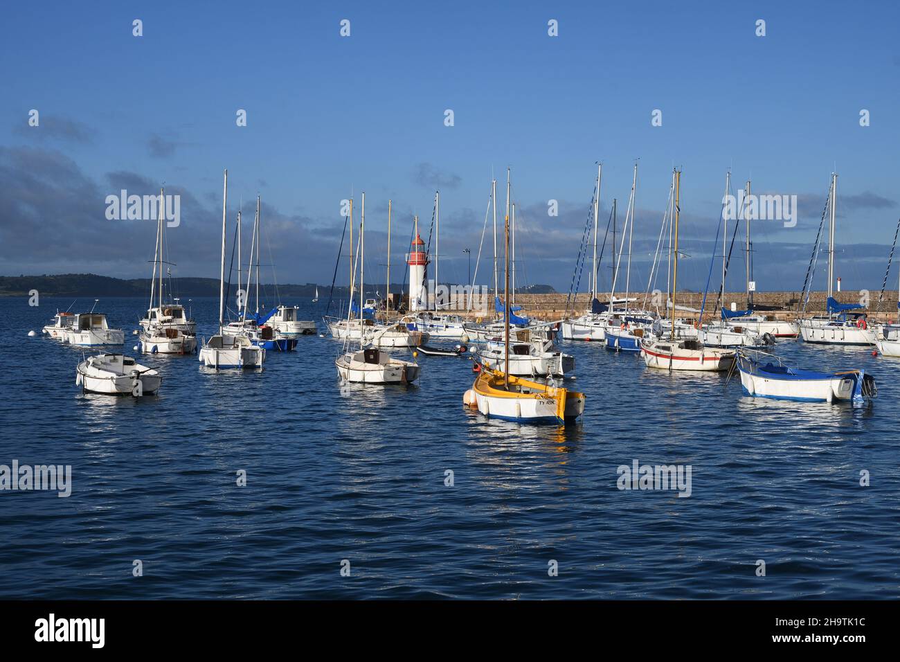 sunlit sailing boats in Erquy harbor, lighthouse in the background , France, Brittany, Departement Cotes-d’Armor, Erquy Stock Photo