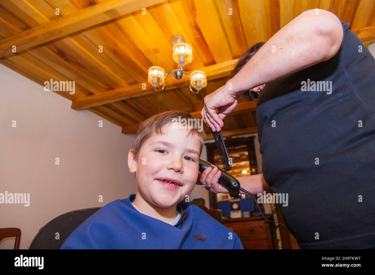 Grandmother cutting hair to his little grandson in her home sewing room. living at home during lockdown. Stock Photo