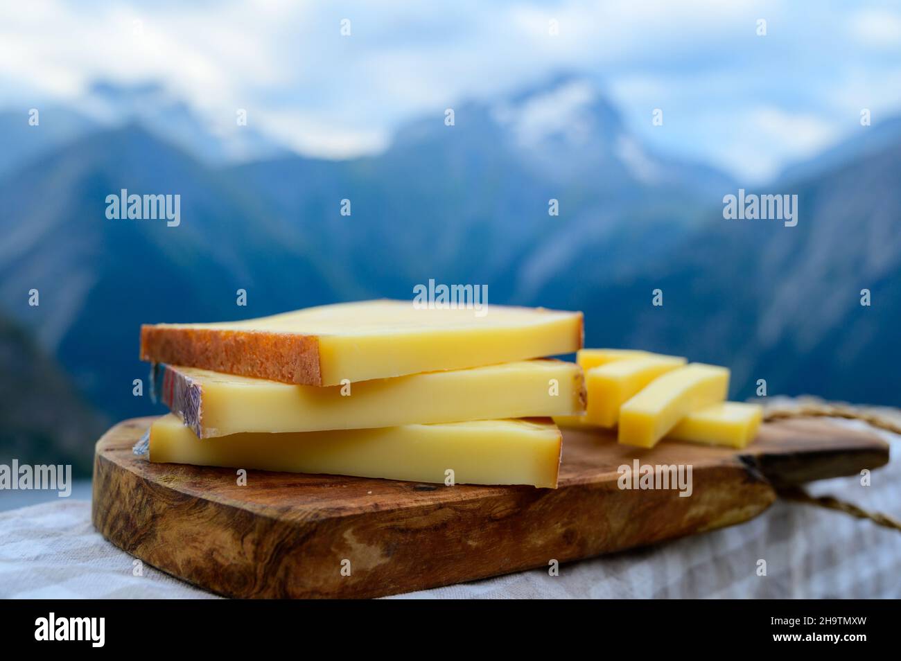 Cheese collection, French comte, beaufort or abondance cow milk cheese served outdoor with Alps mountains peaks in summer on background Stock Photo