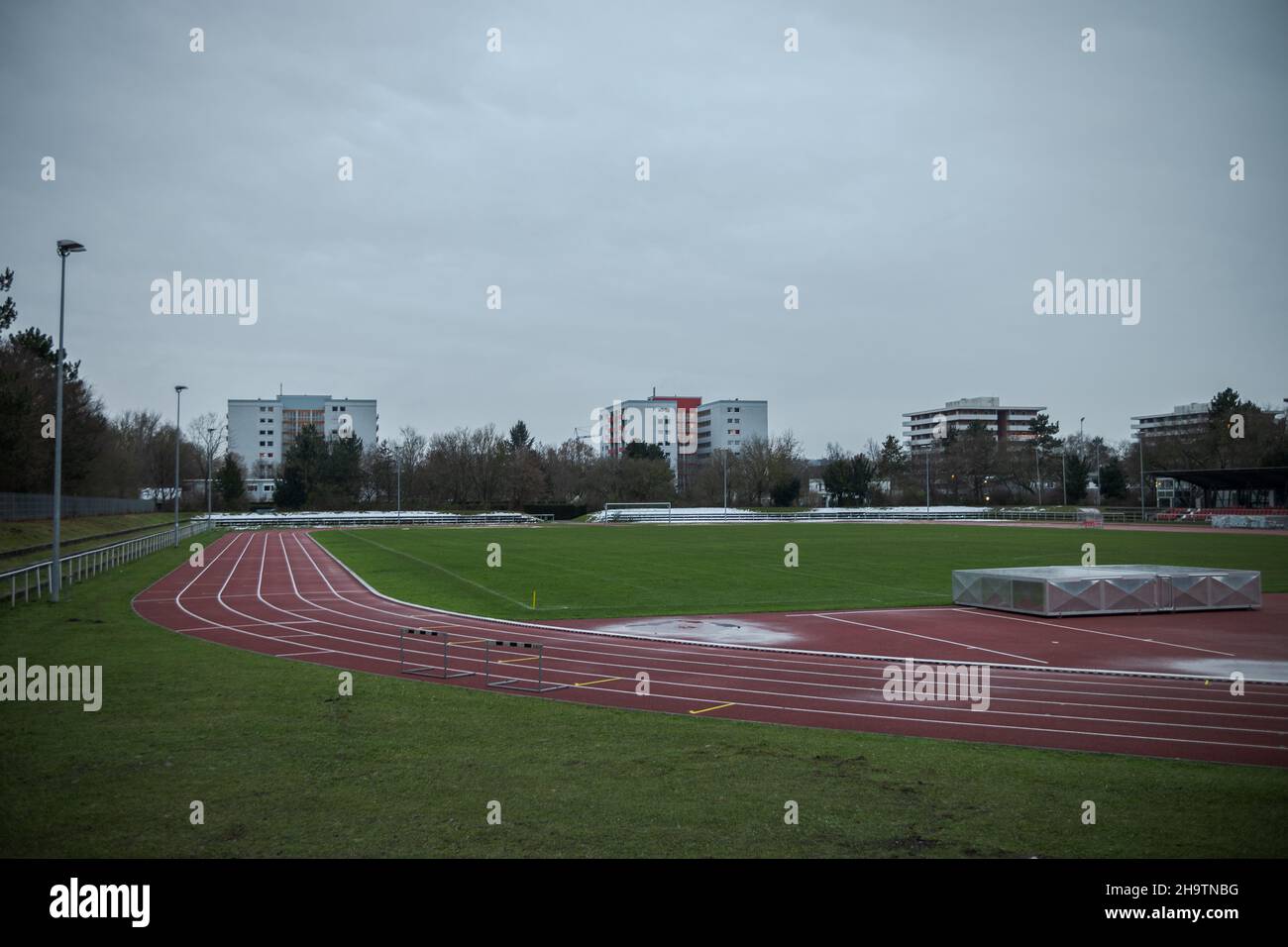 Empty and deserted soccer field and race track in suburban area with flood light poles on grey overcast day with highrise buildings in background Stock Photo