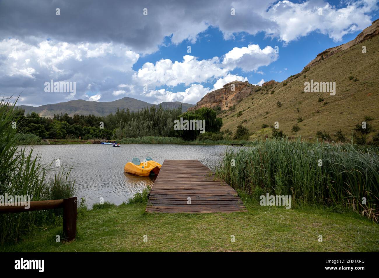 Countryside scene of a wooden jetty with a yellow paddle boat next to it in a lake. There is clouds in the sky Stock Photo