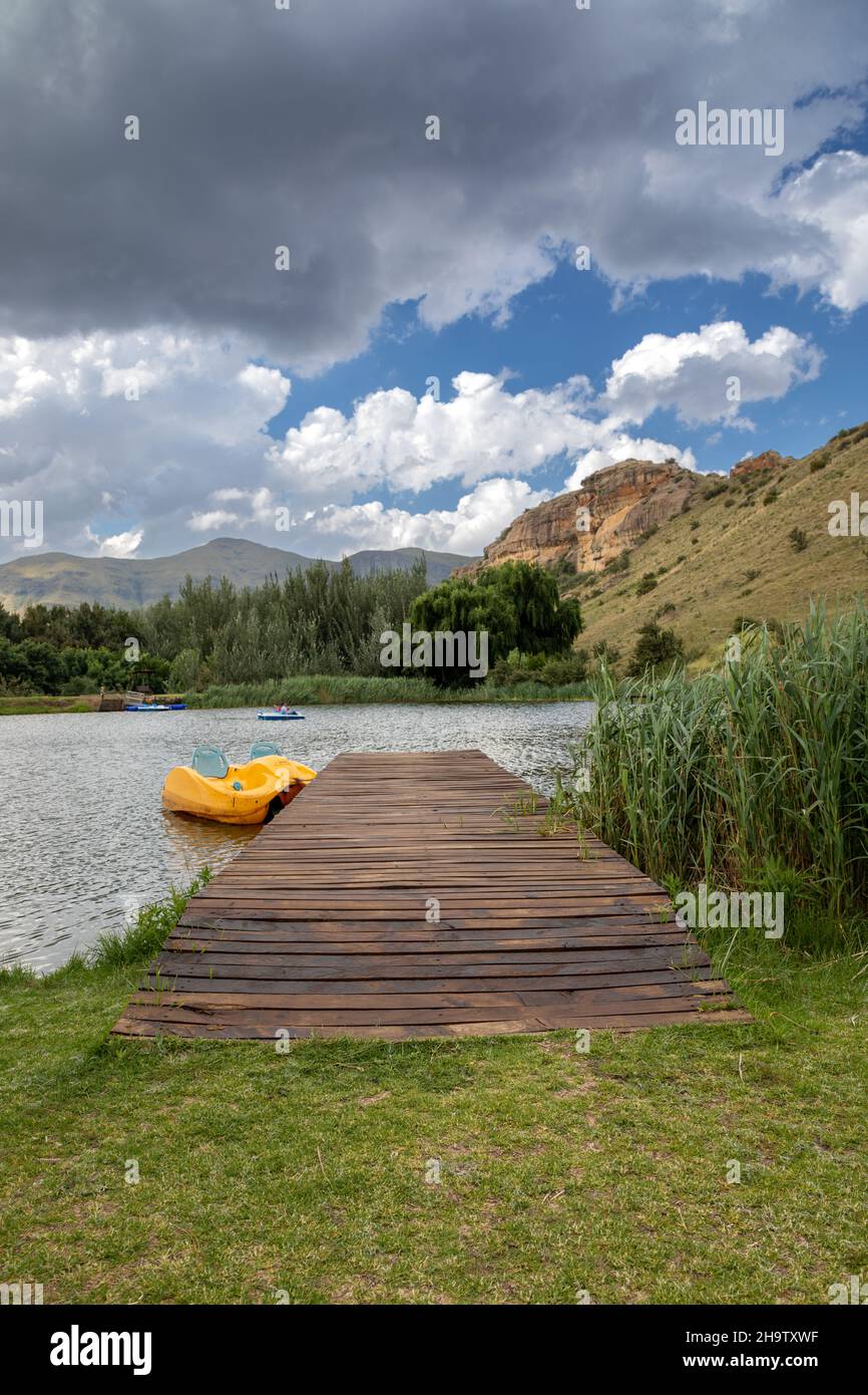 vertical countyside scene of a wooden jetty with a yellow paddle boat next to it in a lake Stock Photo